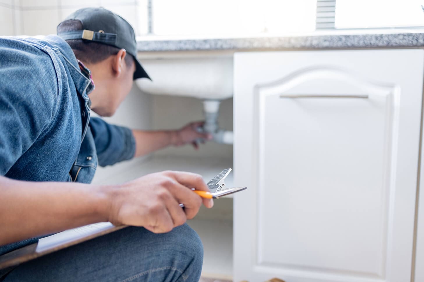 Plumber inspecting kitchen sink plumbing.